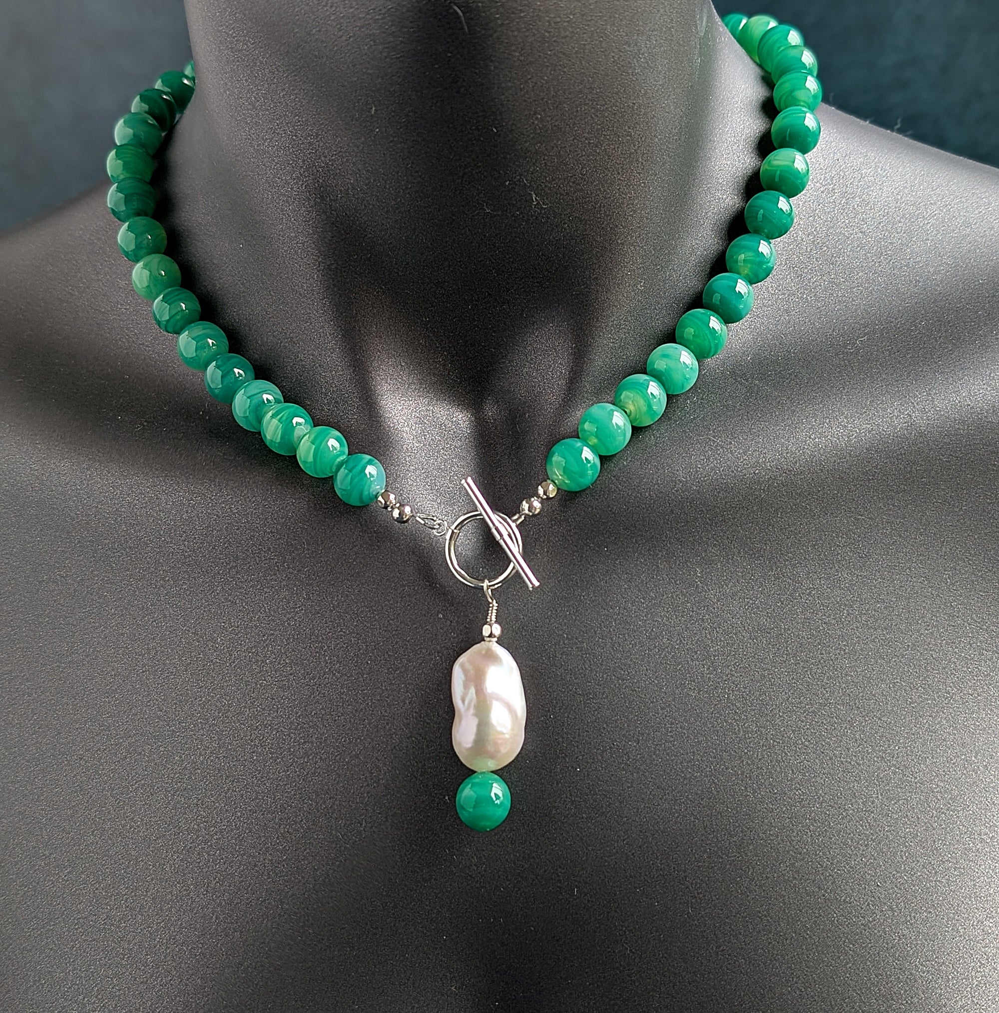 Green beaded necklace with a pearl pendant on a mannequin.