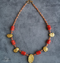Load image into Gallery viewer, Showing the whole Gold and coral necklace with gold toggle clasp. There are five oval, tearshaped gold gilded textured tektite stones. The center stone is larger than the others. Inbetween are six dark orange barrel shaped and oval shaped coral beads with small gold glass beads inbetween and tapering to the clasp measuring 18&quot;.