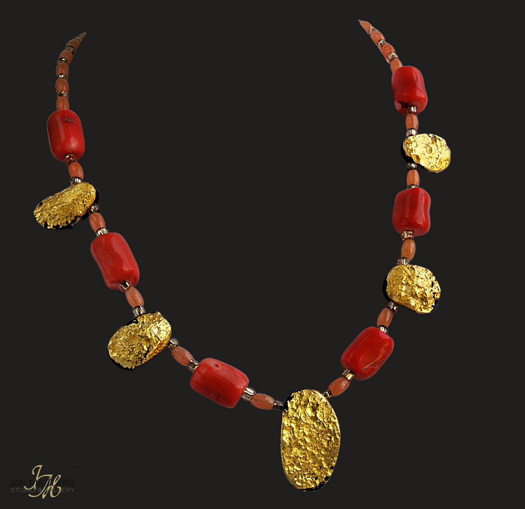 Gold and coral necklace. There are five oval, tearshaped gold gilded textured tektite stones. The center stone is larger than the others. Inbetween are dark orange barrel shaped and oval shaped coral beads with small gold glass beads inbetween.