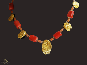 Gold and coral necklace. There are five oval, tearshaped gold gilded textured tektite stones. The center stone is larger than the others. Inbetween are dark orange barrel shaped and oval shaped coral beads with small gold glass beads inbetween.