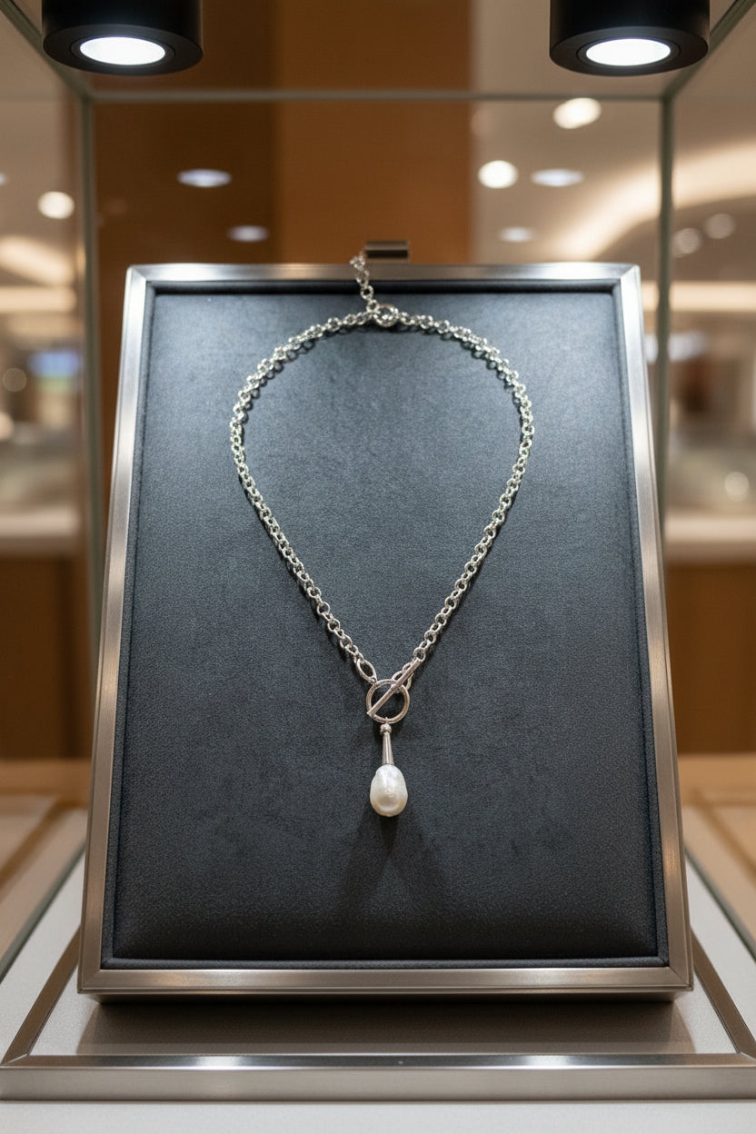 Silver necklace with a pearl pendant on a grey background in a display case.