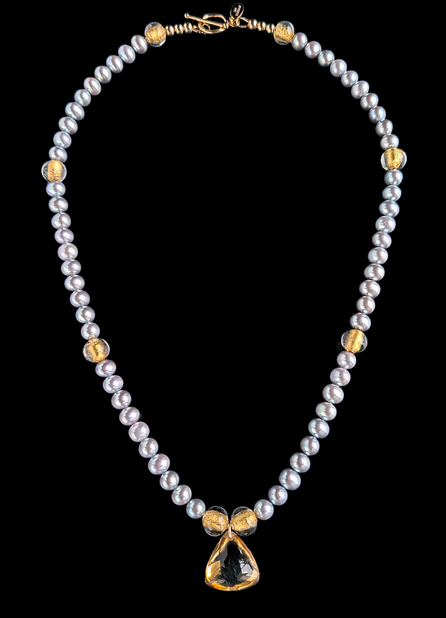 Pearl necklace with gold accents and a central citrine pendant on a black background