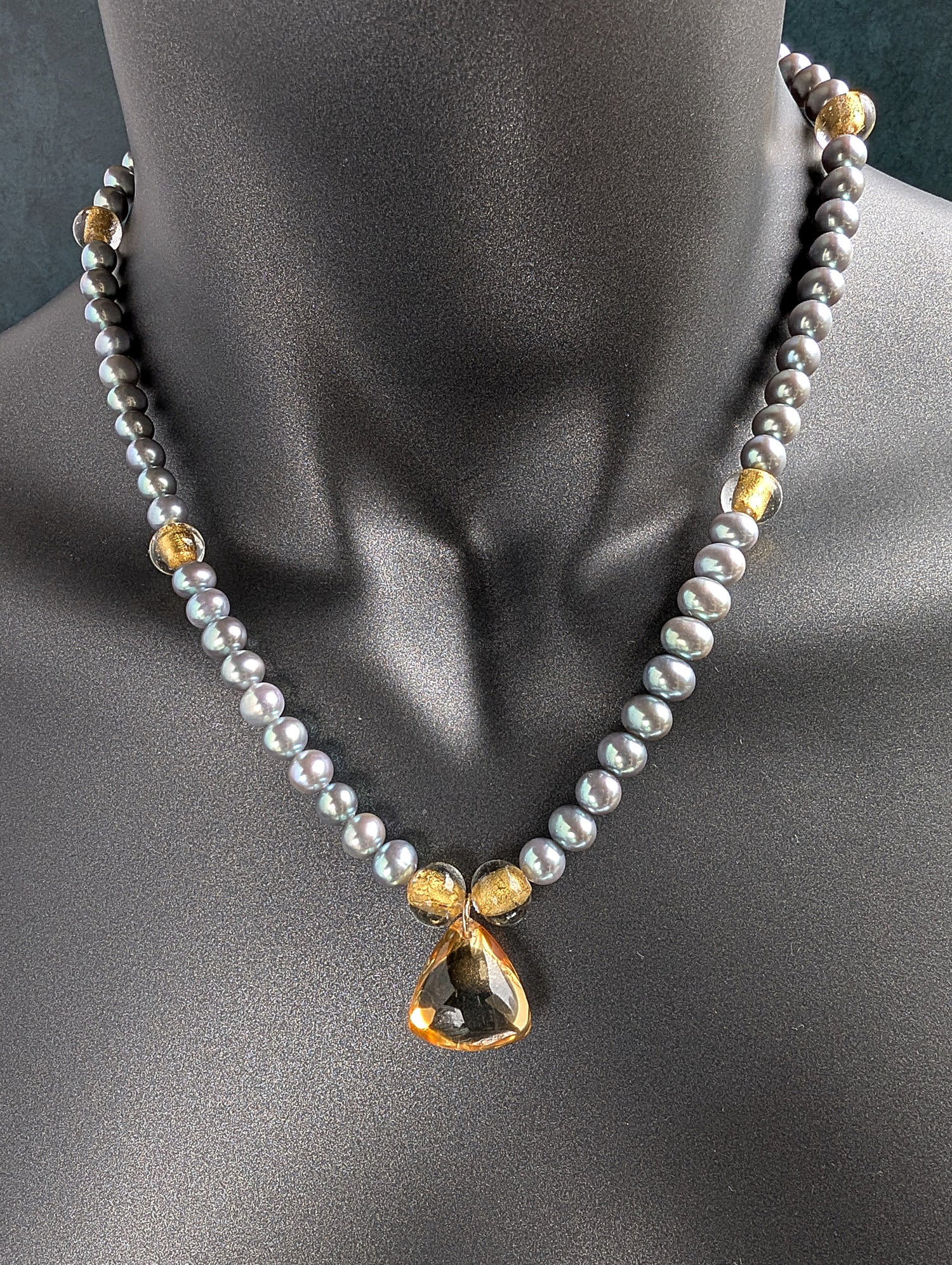 Necklace with gray pearls, citrine pendant and gold accents on a mannequin