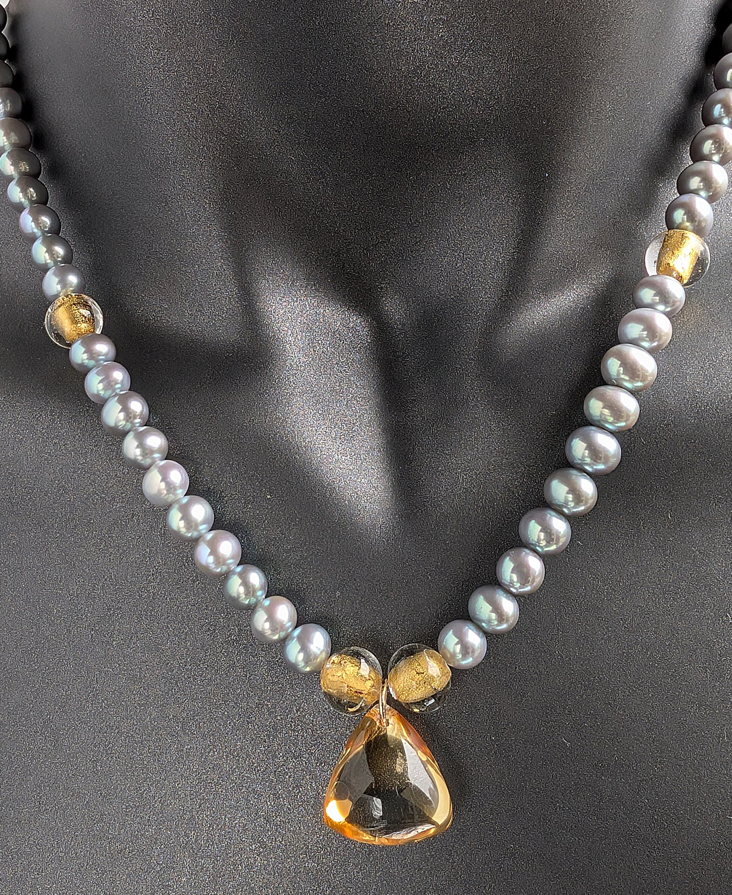 Pearl necklace with a gold clasp on a mannequin bust.