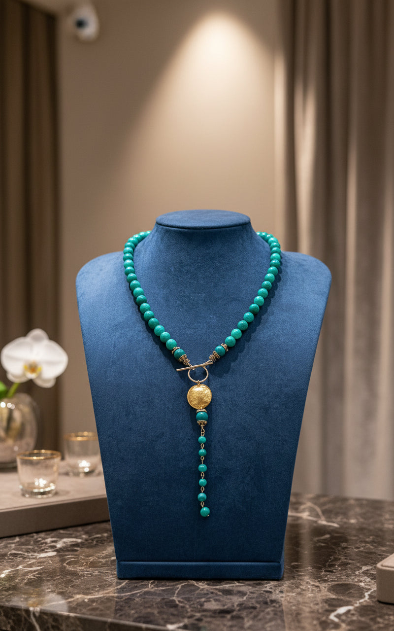 Green lace agate beaded necklace with a gold pendant on a blue display neck. 
