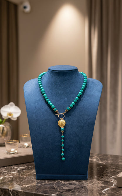 Green lace agate beaded necklace with a gold pendant on a blue display neck. 