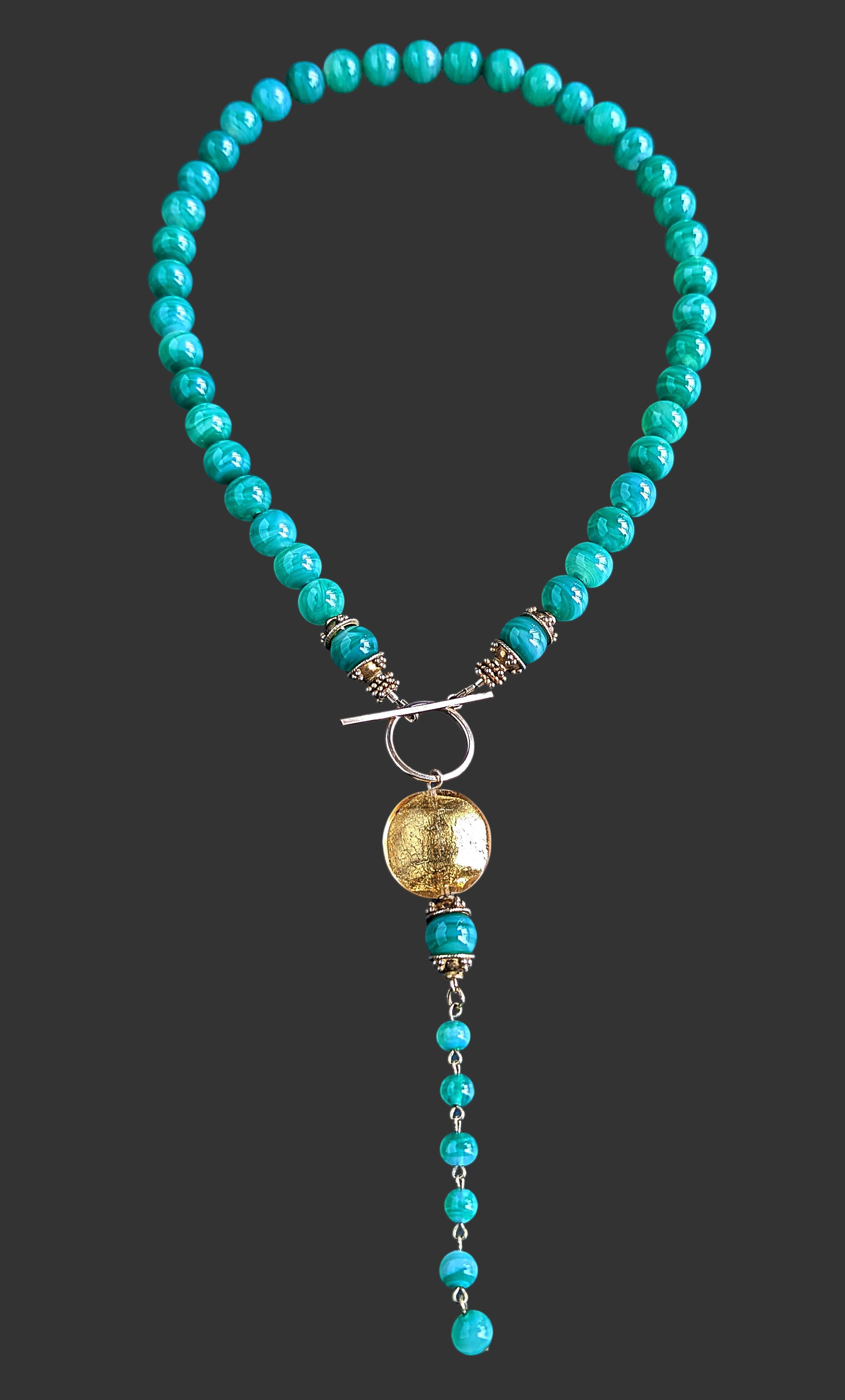 Green beaded necklace with a gold pendant on a black background.