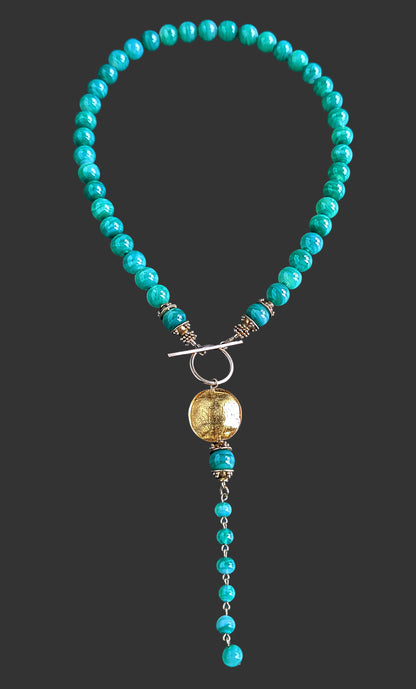 Green beaded necklace with a gold pendant on a black background.