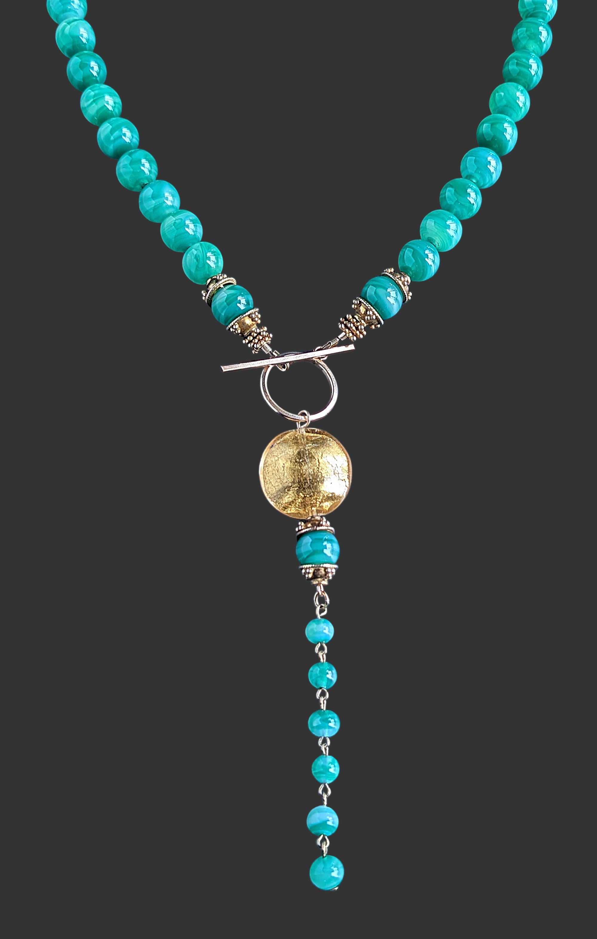 Green beaded necklace with a gold pendant on a black background.