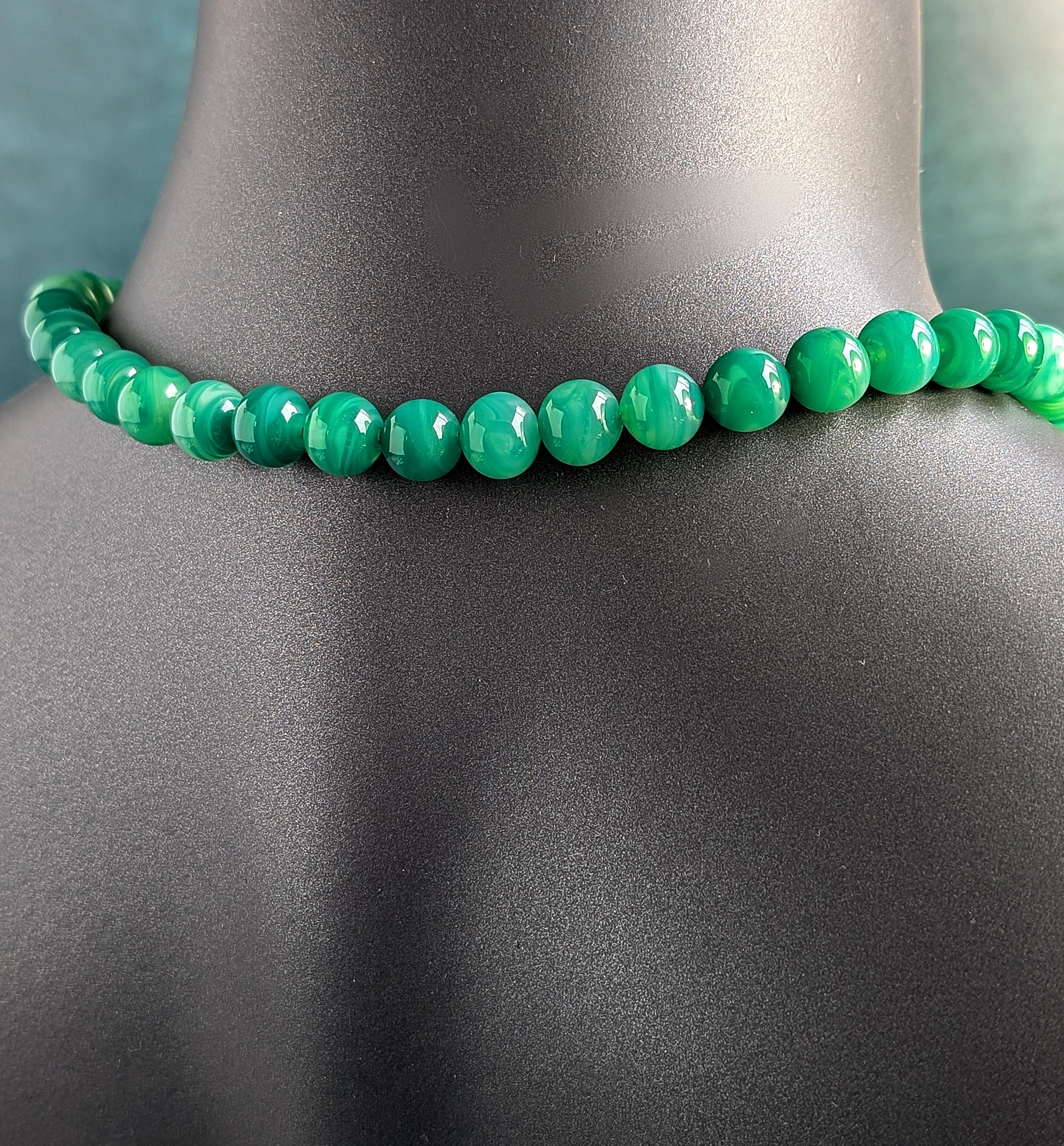 The back of a green beaded necklace on a mannequin neck against a neutral background