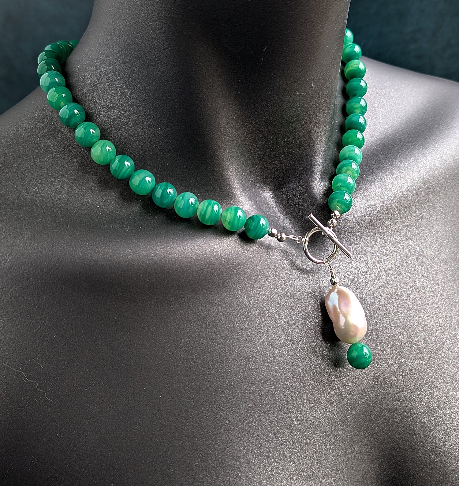 Green beaded necklace with a pearl pendant on a mannequin.