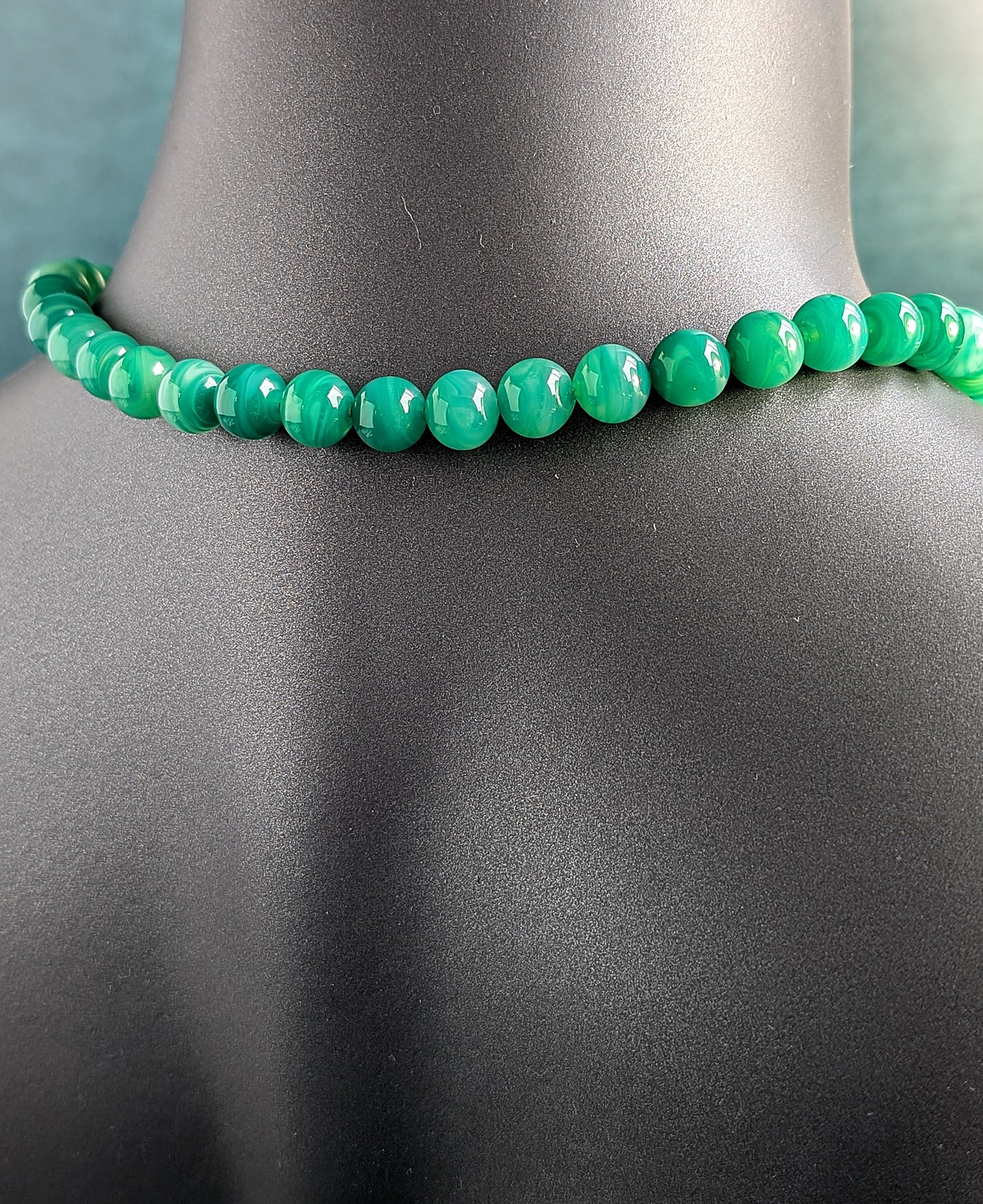 The back of green beaded necklace on a mannequin with a gray background
