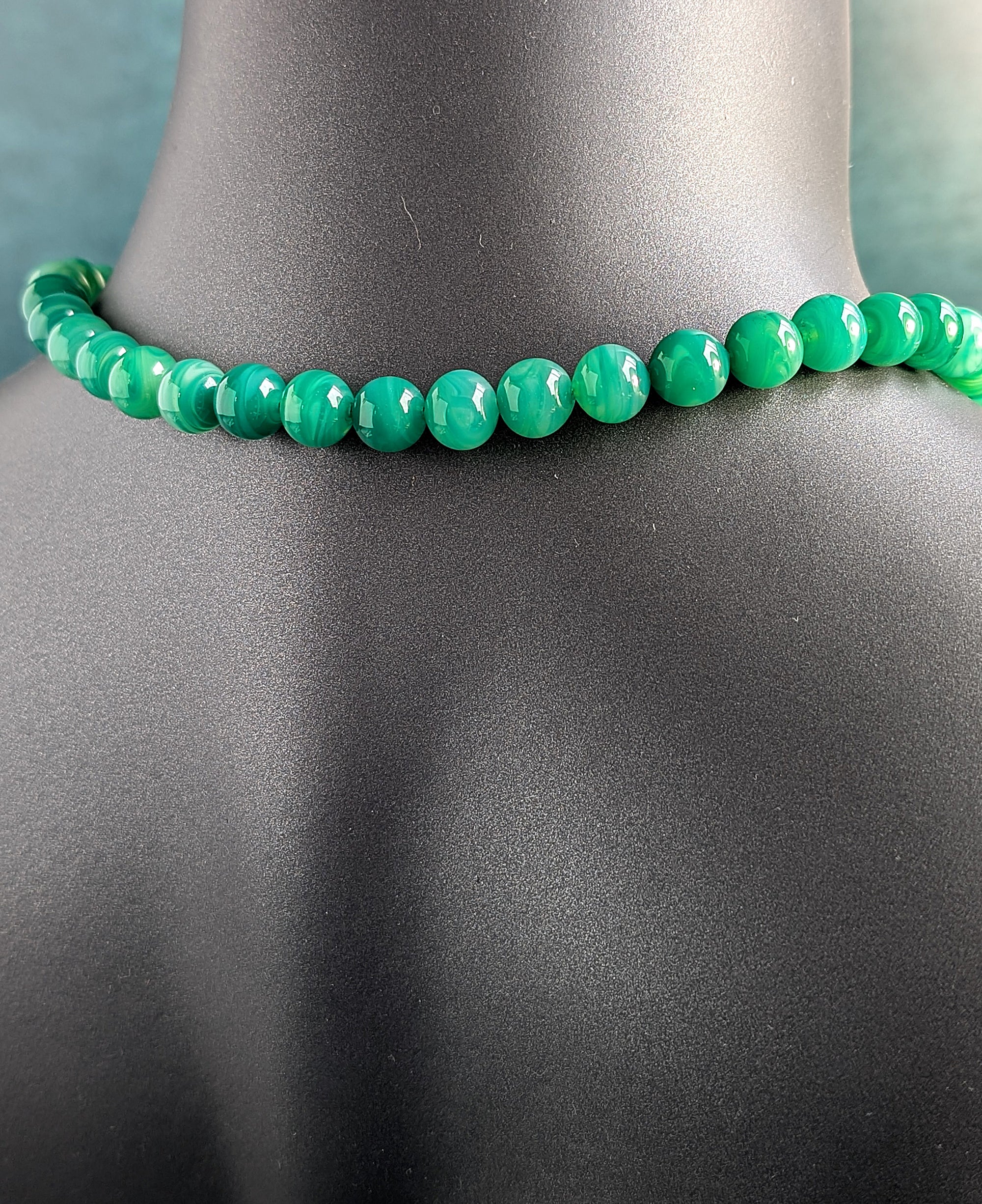 The back of green beaded necklace on a mannequin with a gray background