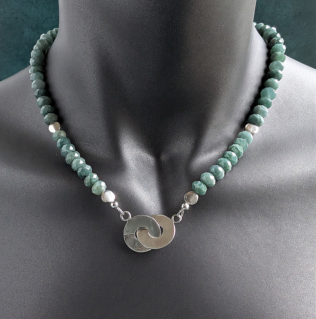 Necklace with green beads and a silver pendant on a mannequin.