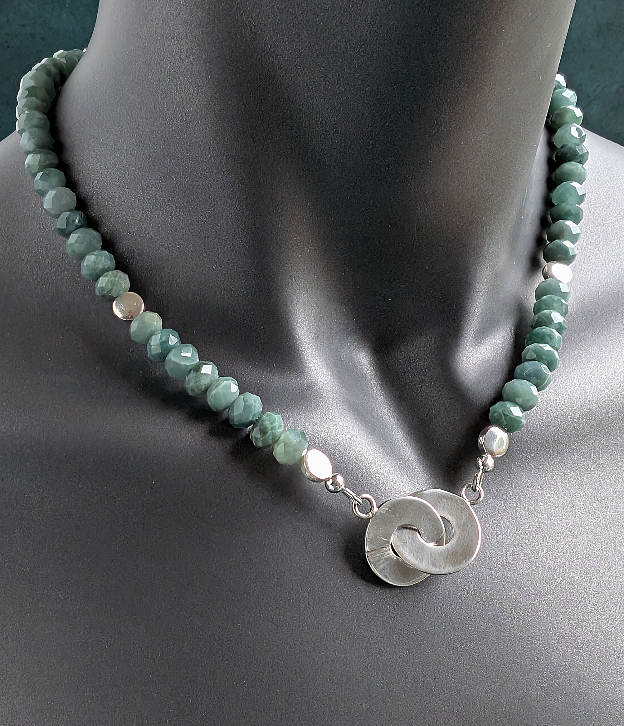Necklace with green beads and a silver pendant on a mannequin.