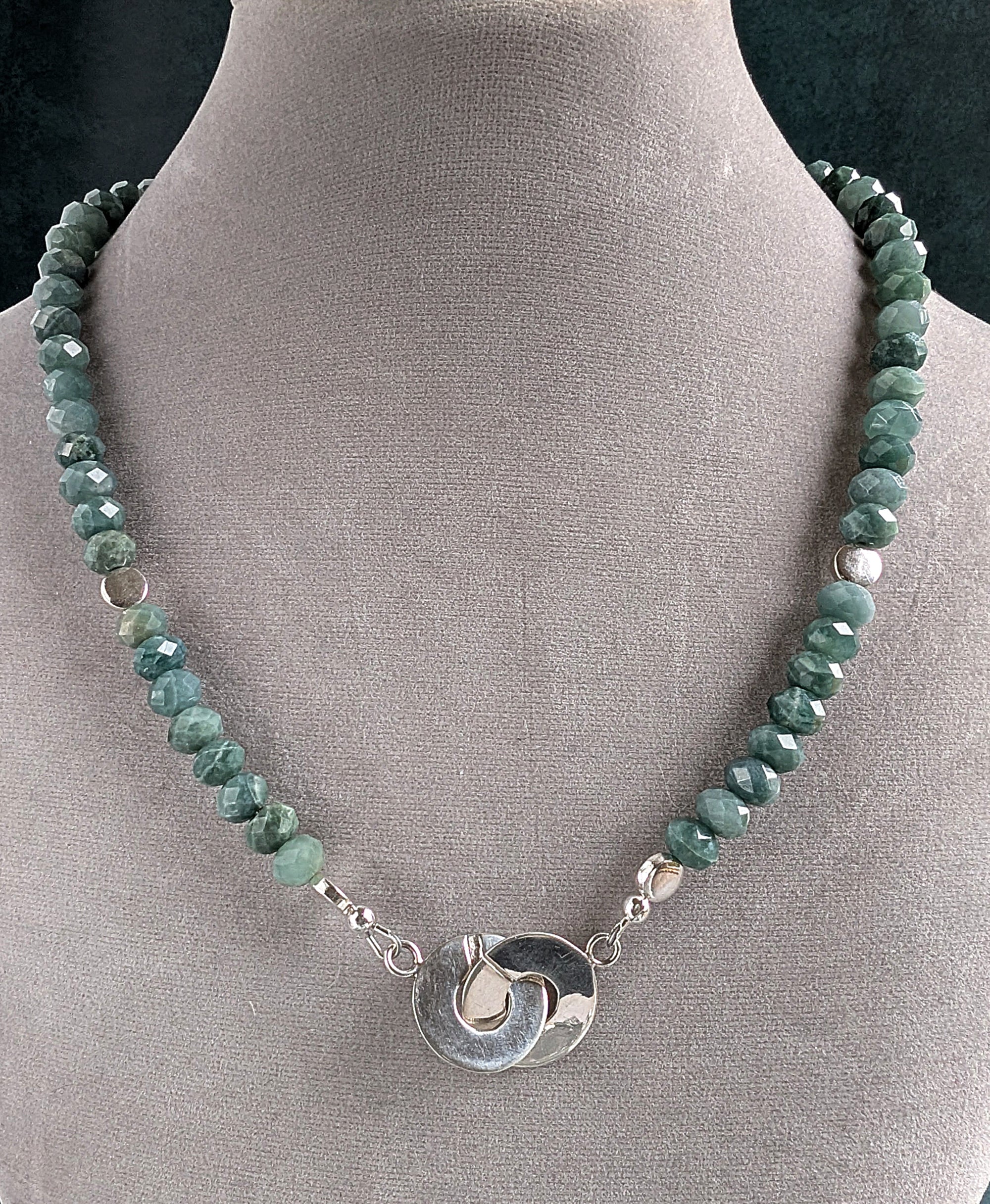 Necklace with green beads and a silver pendant on a gray display neck.