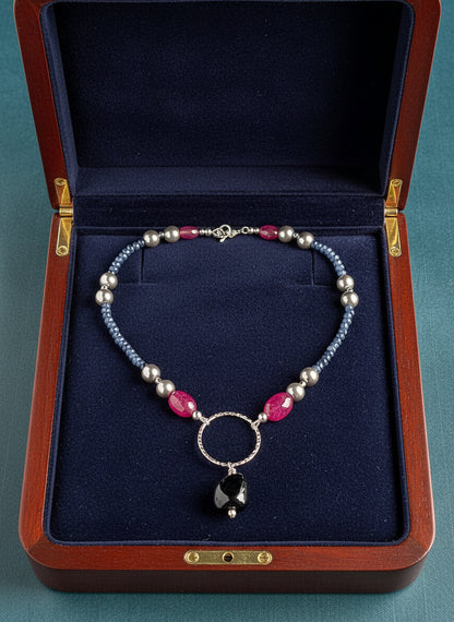 Necklace with blue, rose, and navy beads on a  navy background in a wooden jewelry case.