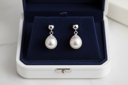 Pair of pearl earrings with silver ball studs on blue velvet and white jewelry box.