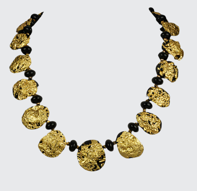 Gold necklace with black onyx beads on a white background.