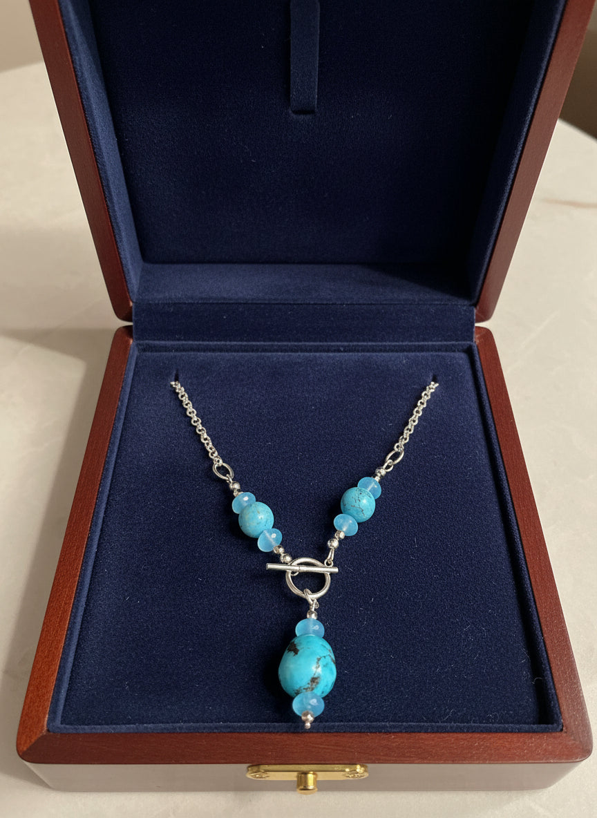 Necklace with turquoise beads and a silver clasp in a navy velvet and wood jewelry box.