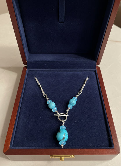 Necklace with turquoise beads and a silver clasp in a navy velvet and wood jewelry box.