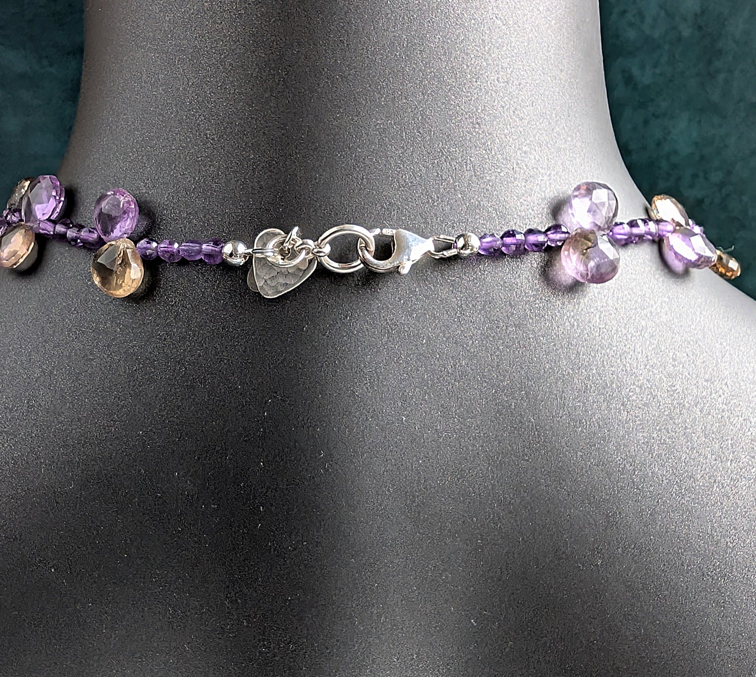 The back silver clasp and  purple beaded necklace on a mannequin with a dark background