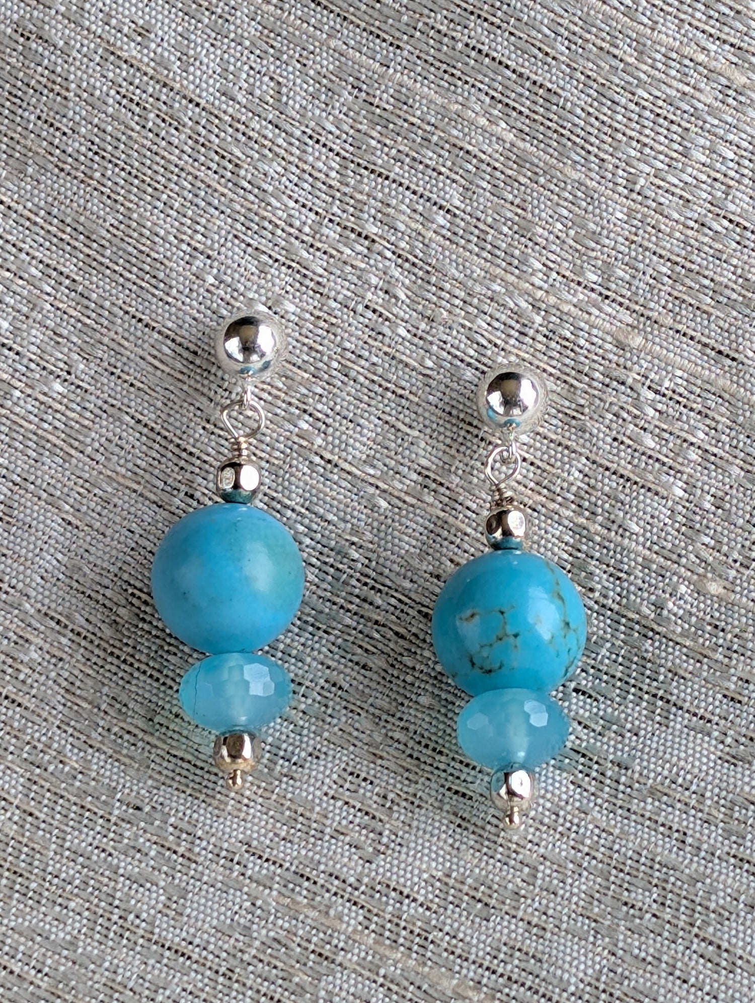 Pair of earrings with blue beads and silver accents on a textured gray background