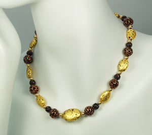 Hand made necklace with 23 karat gold gilded lava stones, lamp work bronze Czech glass, and 14 karat gold filled small round beads. The necklace is finished with 14 karat gold filled toggle clasp. The necklace is photographed on a white mannequin.