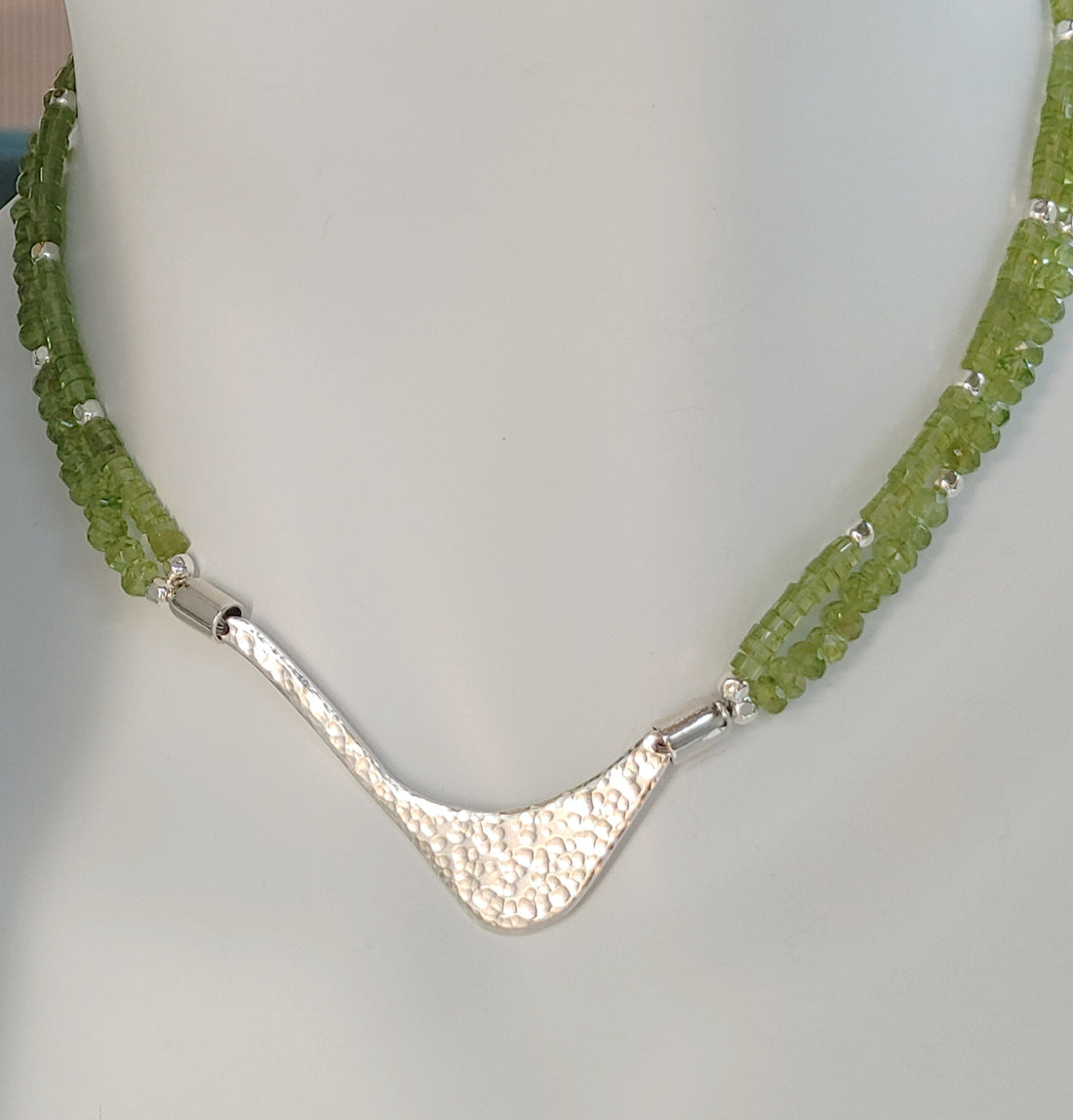 Hammered silver abstract pendant necklace with two strands of peridot and silver beads. The necklace is finished with a magnetic clasp and the artist&