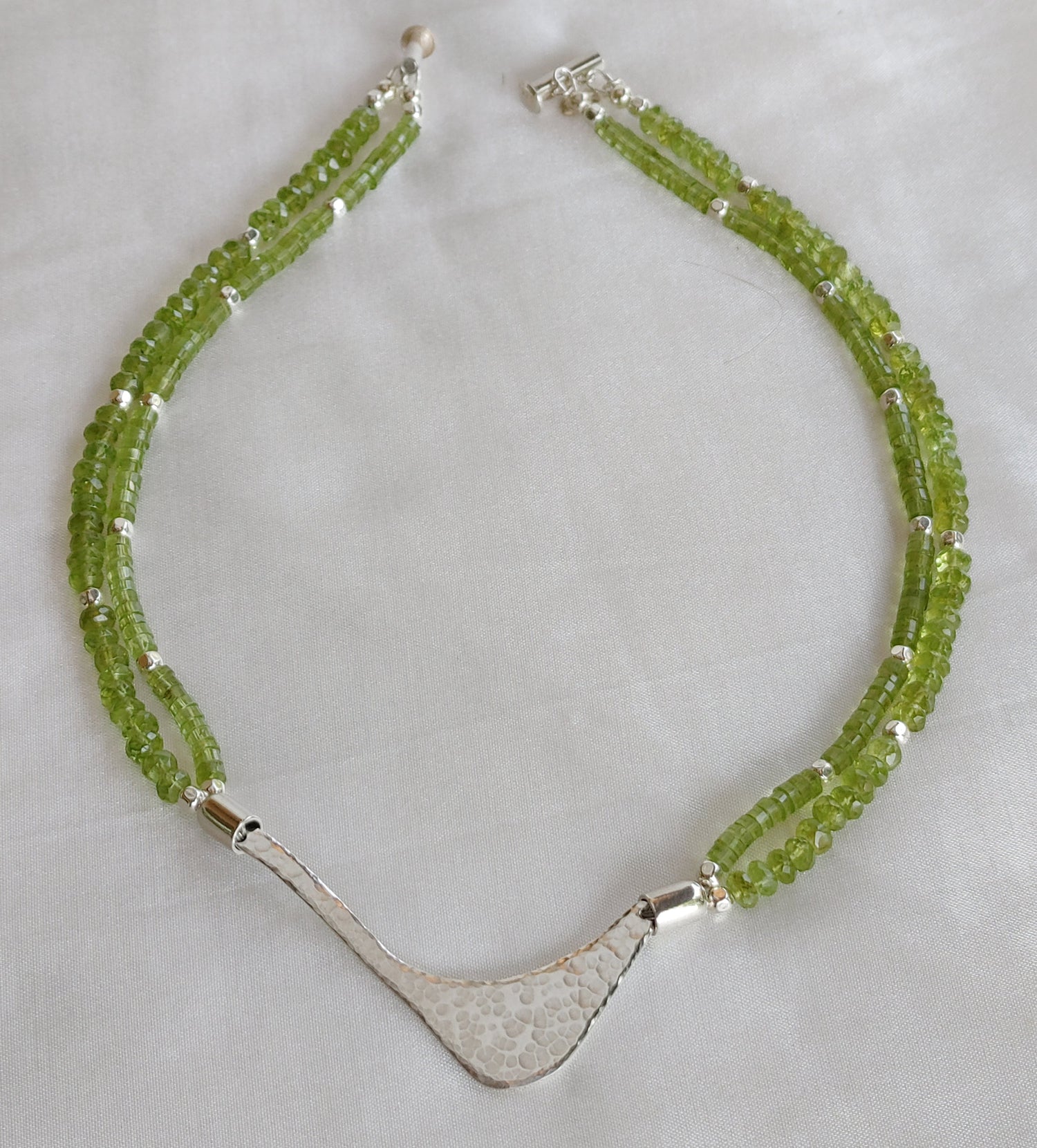 Hammered silver abstract pendant necklace with two strands of peridot and silver beads. The necklace is finished with a magnetic clasp and the artist&