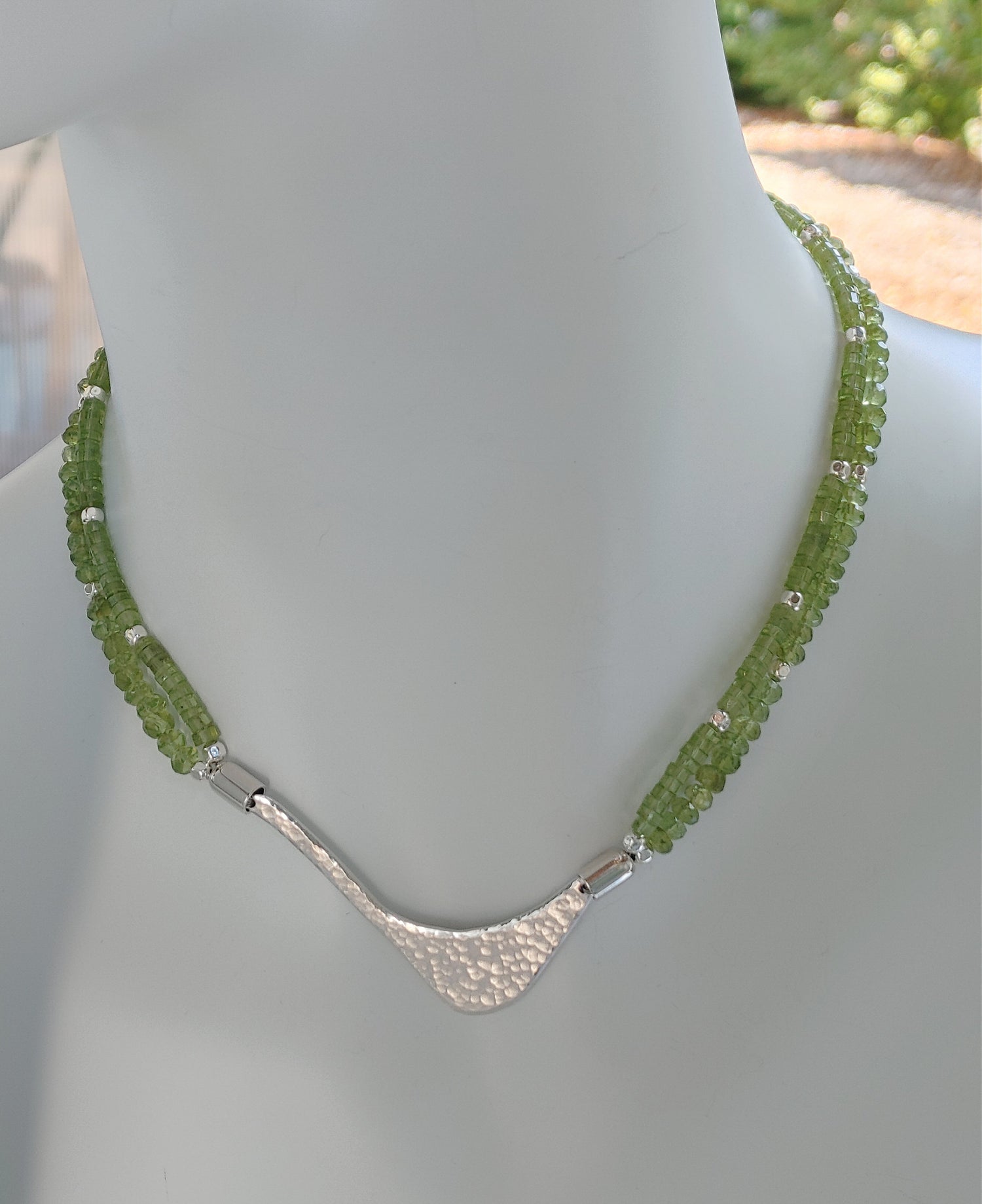 Hammered silver abstract pendant necklace with two strands of faceted peridot and silver beads. The necklace is finished with a magnetic clasp and the artist&